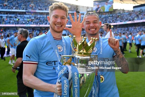 Kevin De Bruyne of Manchester City, gesturing the number five, poses for a photograph with the Premier League Trophy and Kalvin Phillips, gesturing...