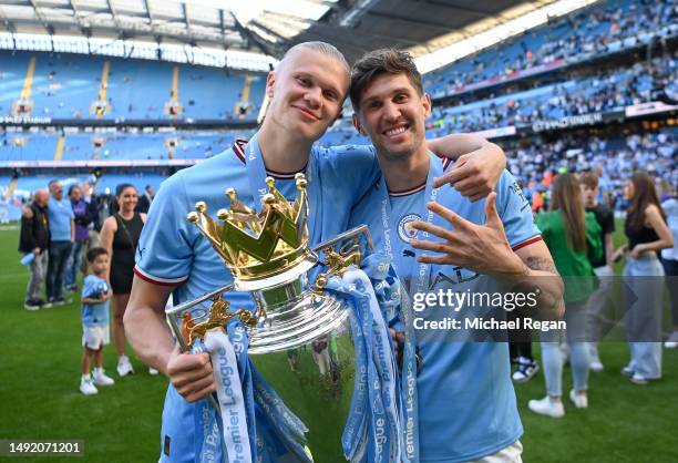 Erling Haaland of Manchester City poses for a photograph with the Premier League Trophy and John Stones, gesturing the number five, following the...