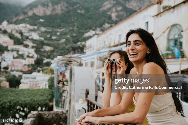 two beautiful woman perch on a railing and look out over the epic view of positano, italy. - indian tour guide stock pictures, royalty-free photos & images