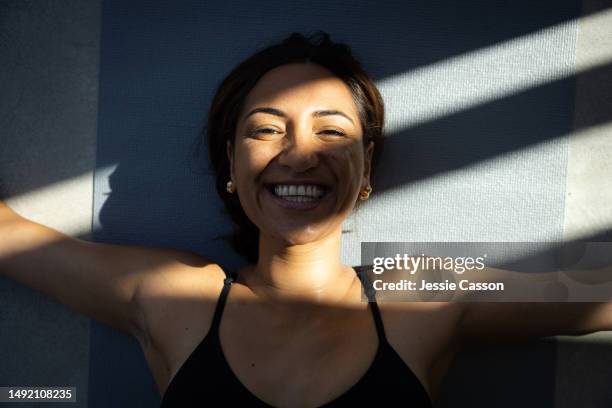 smiling woman lying on yoga mat with arms outstretched - australasia fotografías e imágenes de stock