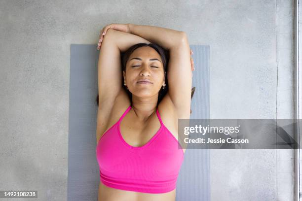 woman lying on yoga mat with arms crossed above head and eyes closed - schlafen sport stock-fotos und bilder