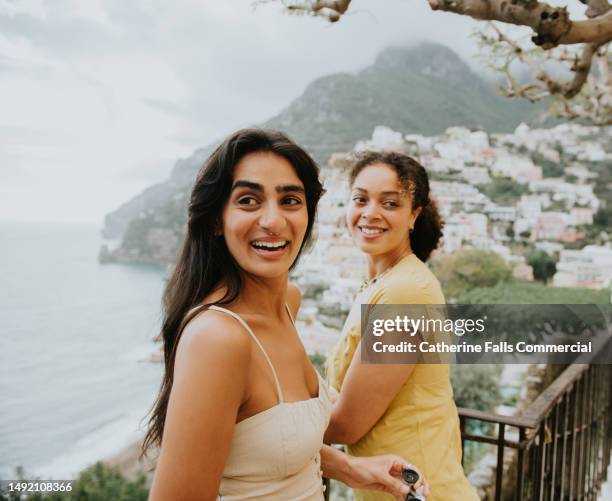 two beautiful, happy woman perch on a railing in positano, italy. - mediterranean stock-fotos und bilder