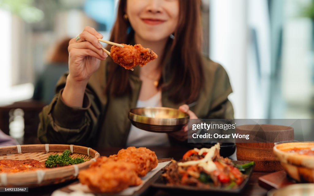Chopped shot of young Asian woman eating fried chicken with chopsticks in a Korean restaurant
