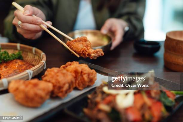 cropped shot of female eating korean fried chicken with chopsticks in the restaurant - korean culture stock pictures, royalty-free photos & images