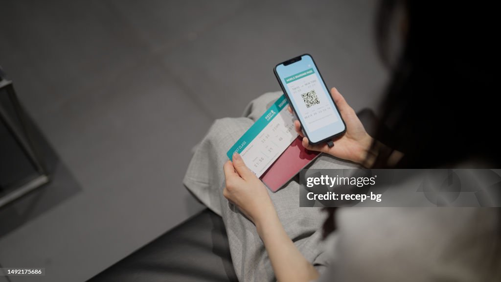 Businesswoman checking her digital boarding app on smart phone and her plane ticket
