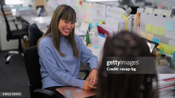 two multi-ethnic businesswoman talking casually with each other in modern office - effortless experience stock pictures, royalty-free photos & images