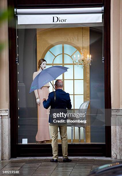 Pedestrian shelters under an umbrella as he looks in the window of a Christian Dior SA store on Maximilianstrasse in Munich, Germany, on Wednesday,...