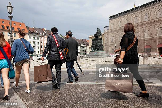 Pedestrians carry Louis Vuitton and Gucci shopping as they cross Max-Joseph Platz in Munich, Germany, on Wednesday, July 25, 2012. Spending at German...