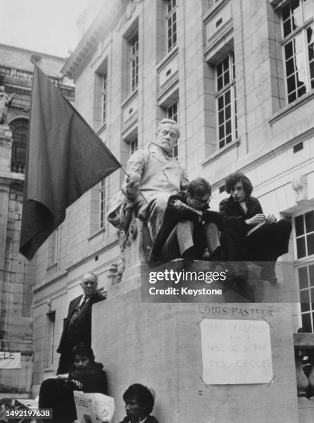 Students sitting on the plinth of the statue of Louis Pasteur, which has the red international flag placed in its hand, part of the May 1968 protests...