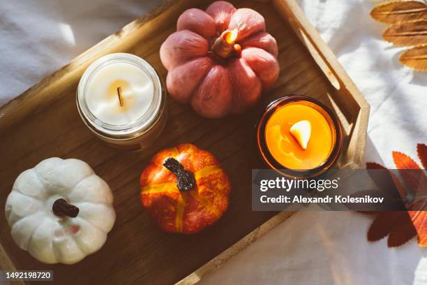 wooden tray with atmospheric soy candles and candles in glass, autumn fall leaves on white bed. autumn cozy home and hygge concept - candle overhead stock-fotos und bilder