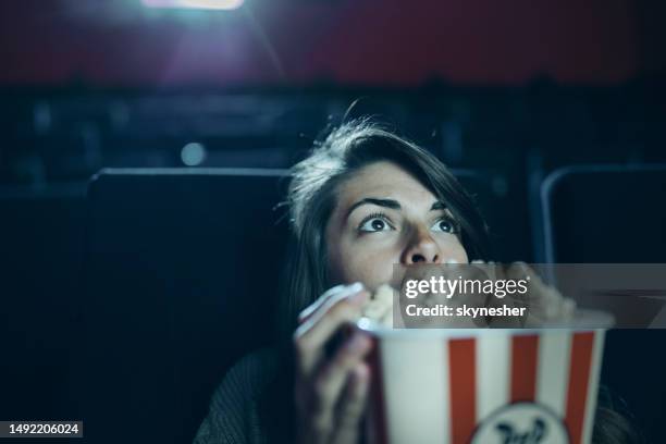 mujer temerosa comiendo palomitas de maíz mientras ve una película en el cine. - when we were young and afraid opening night fotografías e imágenes de stock