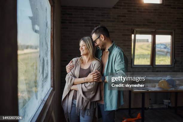 feliz pareja disfrutando junto a la ventana en su nuevo hogar. - relación humana fotografías e imágenes de stock