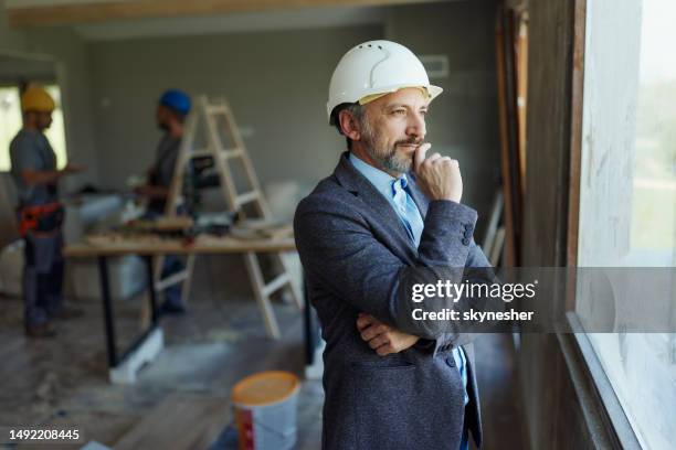 pensive male architect by the window during home renovation. - real estate developer stock pictures, royalty-free photos & images