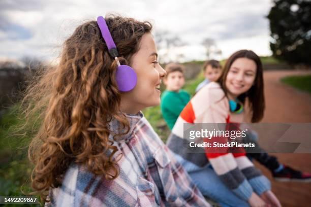 gruppe von teenagern, die sich unterhalten, während sie im park sitzen - young boy enjoying music stock-fotos und bilder