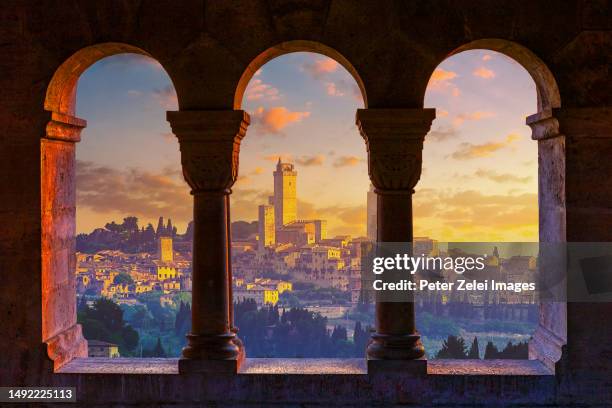 view of san gimignano through an old stone window at sunrise - san gimignano stock-fotos und bilder