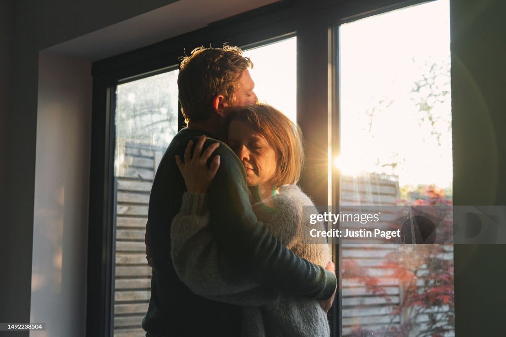 Powerful shot of a mature couple cuddling by the window in the late afternoon sun - emotional support