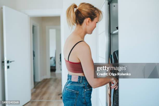 decluttering and excess clothes reduction.  blonde woman picking out her clothes in wardrobe at home - tank top back stock pictures, royalty-free photos & images