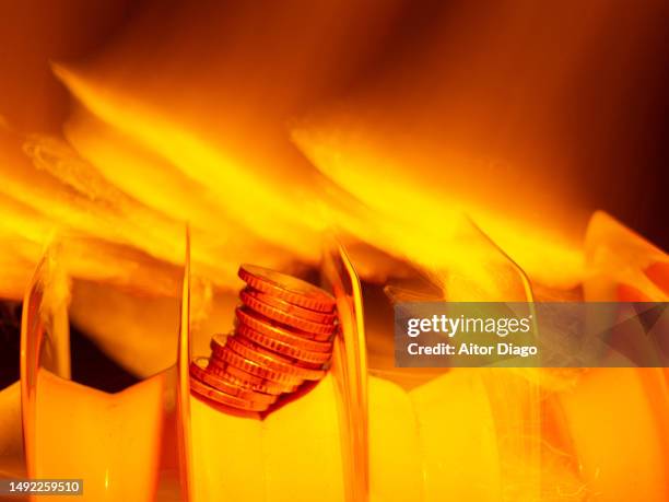 concept of energy costs. creative image of an electric radiator with some coins on it  surrounded by flames. - winter and warm glow stock-fotos und bilder