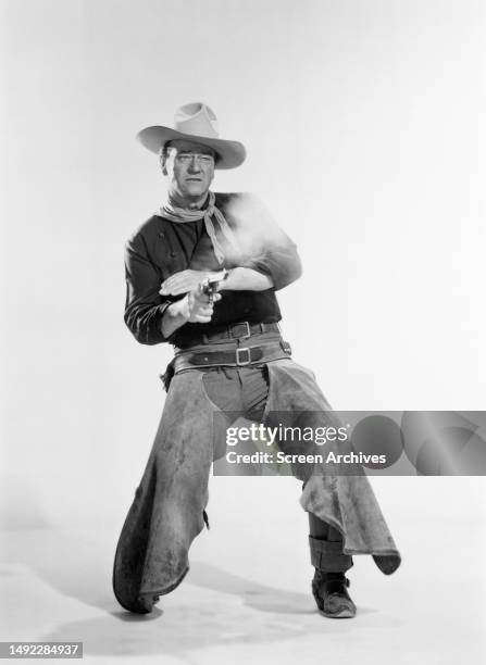 John Wayne in a publicity portrait for the 1962 John Ford western 'The Man Who Shot Liberty Valance' firing gun.