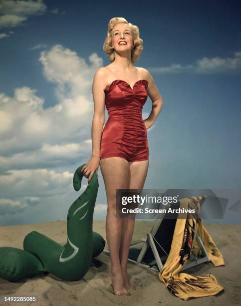 Jan Sterling color red swimsuit 1940's glamour pose of the star posing on studio beach set barefoot.