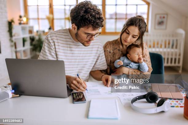 young family with cute little baby boy going over finances at home - financiële planning stockfoto's en -beelden