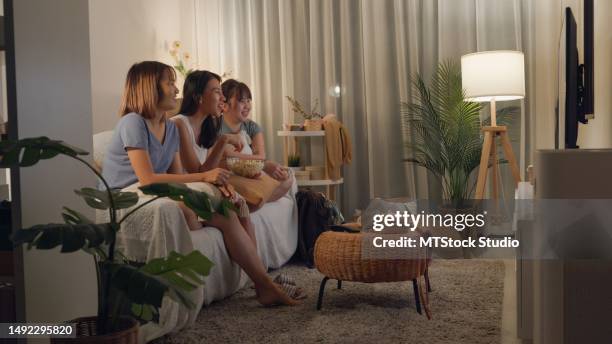 junge asiatische frauen freunde auf dem sofa essen popcorn lustig lachen sehen comedy channel film oder sitcoms show im fernsehen im streaming online zu hause in der nacht. freizeitaktivität, lifestyle. - friends tv show stock-fotos und bilder