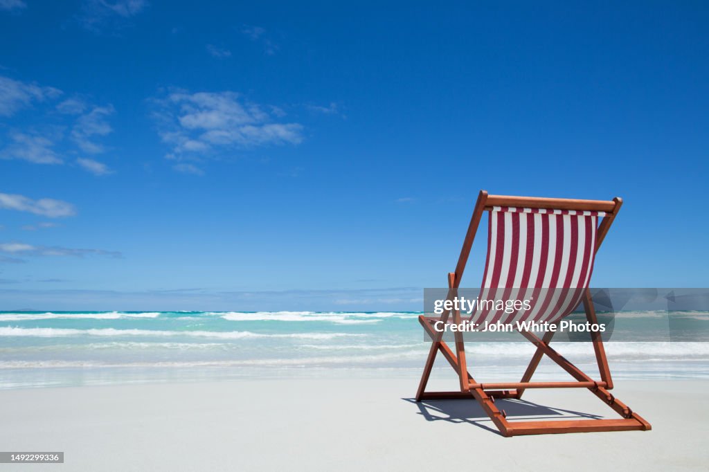 Red and white striped deck chair on an empty beach. Waves and the ocean in the background. Seaside seascape. Blue sky with copy space.