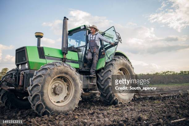 agriculteur âgé conduisant un tracteur dans un champ agricole - agriculteur conducteur tracteur photos et images de collection