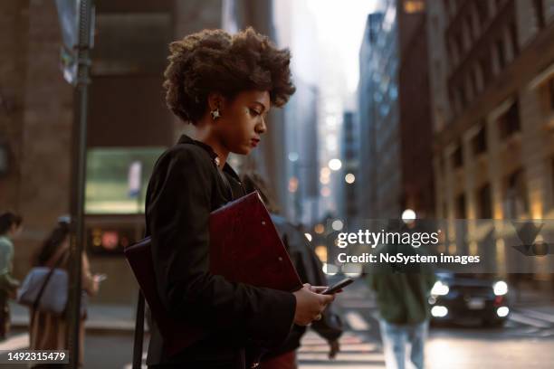 efficient and focused: busy black professional awaits taxi, managing documents and email - businesswoman nyc stock pictures, royalty-free photos & images