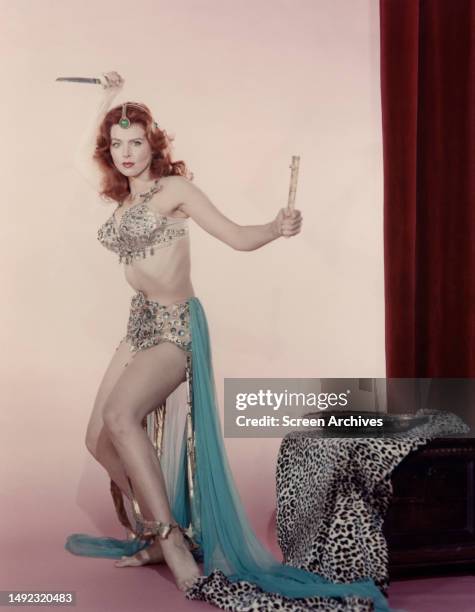 Tina Louise poses in belly dancer costume holding dagger, 1950s.