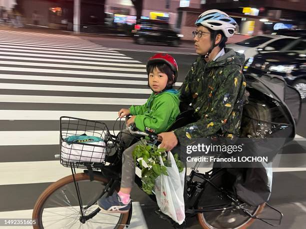 Un homme circule avec un vélo électrique avec un enfant sur le porte-bagage et un autre devant le 10 mai 2023 à Tokyo.