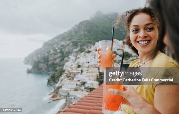 two woman enjoy cocktails on a balcony overlooking positano, italy - mediterranean climate stock pictures, royalty-free photos & images