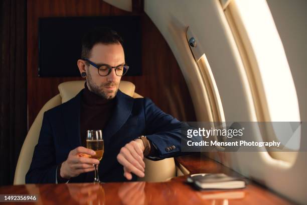 elegant businessman drinking champagne looking through corporate airplane jet window - millionnaire ストックフォトと画像