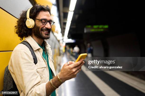 man using smartphone and headphones waiting at subway train station - auscultador equipamento áudio imagens e fotografias de stock