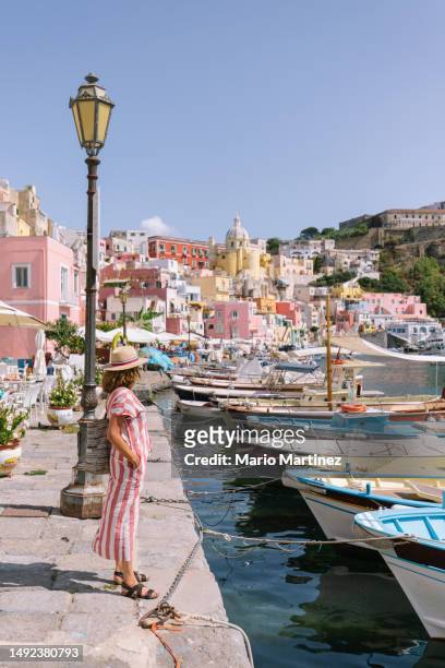 mature woman looking at old boats moored on embankment against procida old town - naples italy church stock pictures, royalty-free photos & images