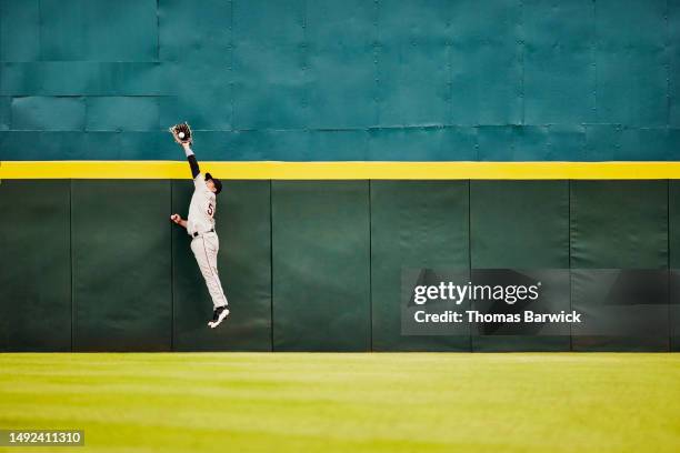 wide shot baseball player jumping for catch at stadium outfield wall - baseball sport stock pictures, royalty-free photos & images