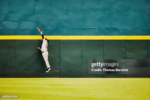 wide shot baseball player jumping for catch at stadium outfield wall - taking a shot - sport imagens e fotografias de stock