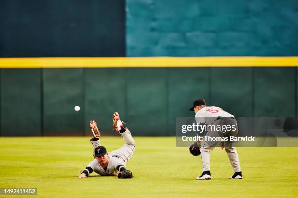 wide shot outfielder diving and missing catch during baseball game - futility stock pictures, royalty-free photos & images