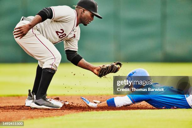 medium wide shot runner sliding into second base during baseball game - base artículos deportivos fotografías e imágenes de stock