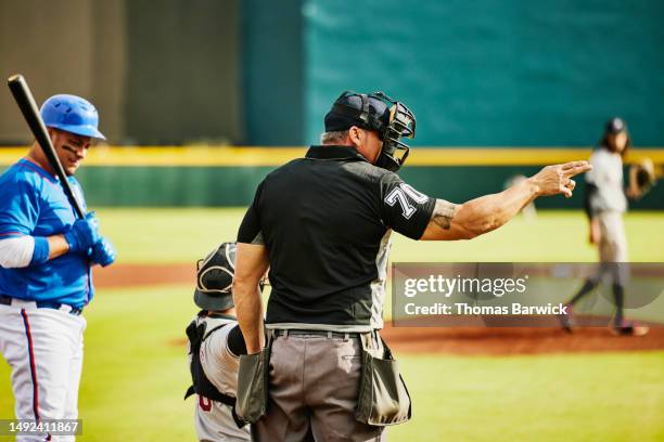 medium wide shot home plate umpire calling strike during baseball game - casque de baseball photos et images de collection