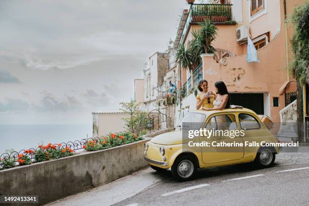 wide shop of two woman in a small, open topped, vintage yellow car. - positano italy stock pictures, royalty-free photos & images