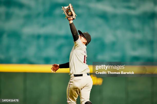 medium wide shot of outfielder reaching for catch during baseball game - catch 22 foto e immagini stock