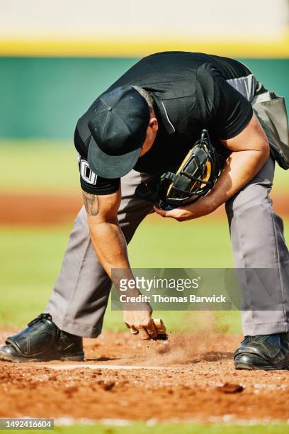 medium wide shot baseball umpire sweeping off home plate during game - baseball umpire stock pictures, royalty-free photos & images