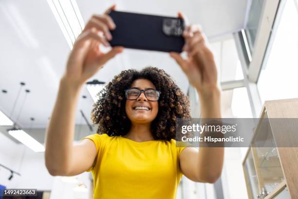 woman buying glasses at an eyewear shop and taking a selfie - cell phone mirror stock pictures, royalty-free photos & images