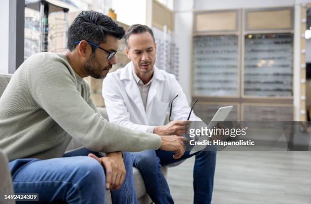 optician performing an eye exam on a man while wearing glasses - doctor and digital tablet stock pictures, royalty-free photos & images