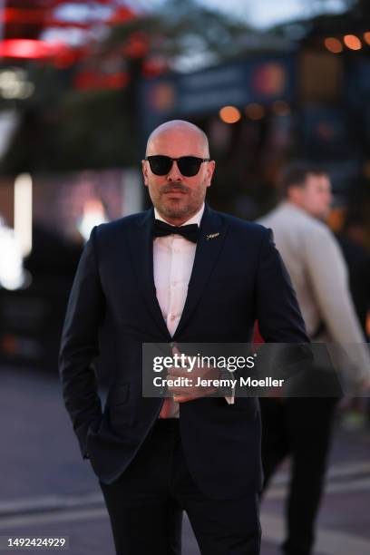 Mathieu Castanier seen wearing a black and white suit, black pants, black bow tie and black sunglasses and red shoes during the 76th Cannes film...