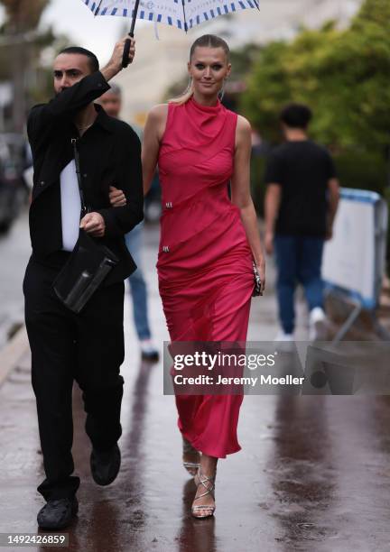 Toni Garrn seen wearing a red long dress with silver mini details, silver long earrings, silver shimmery high sandals and a black mini clutch during...