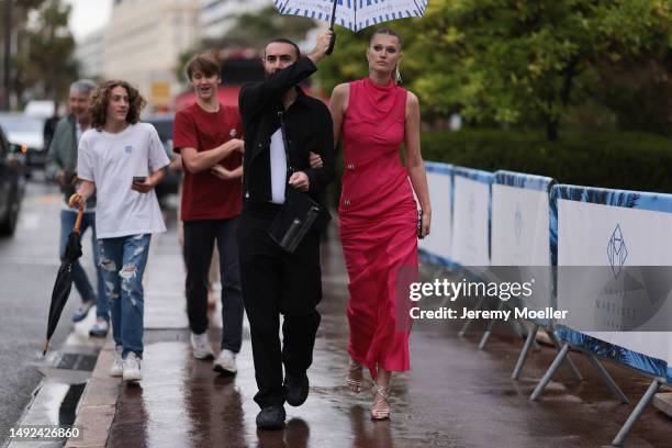 Toni Garrn seen wearing a red long dress with silver mini details, silver long earrings, silver shimmery high sandals and a black mini clutch during...