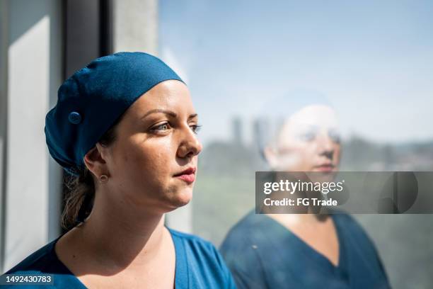 dottoressa contemplativa che guardava pensava alla finestra dell'ospedale - dedizione foto e immagini stock