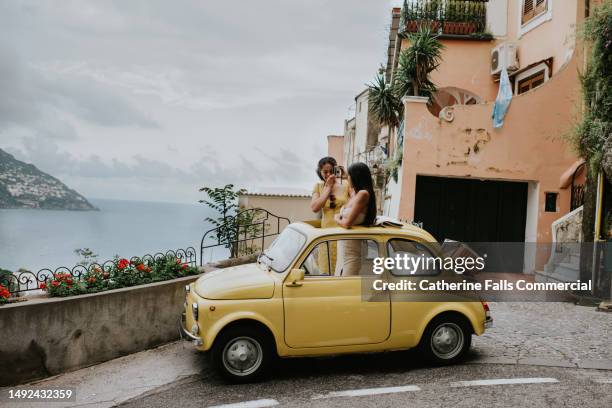 wide shot of two woman in a small, open topped, vintage yellow car. - explorador imagens e fotografias de stock